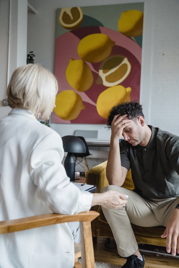 A young man in therapy expressing stress and concern during a session with a psychologist in an indoor setting.